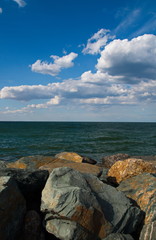Romantic seaside landscape with grey and brown rocks, the green sea and the blue, cloudy sky on a sunny summer day 