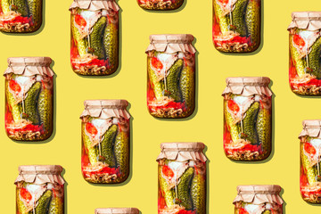 Canned and preserved vegetables in glass jars on yellow background. Pickled cucumbers in jar pattern. Top view. Flat lay. Creative packing design. Healthy fermented food concept