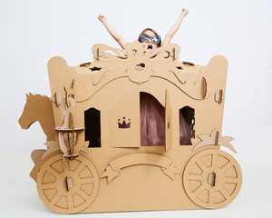 Little princess in crown 7 years old play in carriage made of brown cardboard