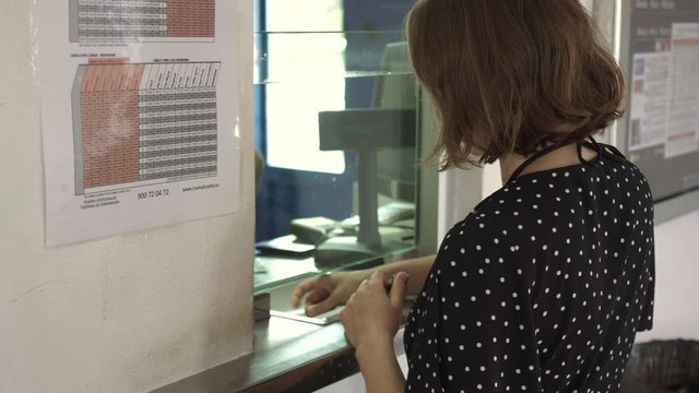 Woman buying a ticket at ticket office and putting change in wallet