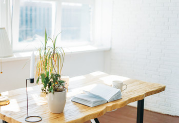 Wooden table with an open book by window in bright room Scandinavian interior