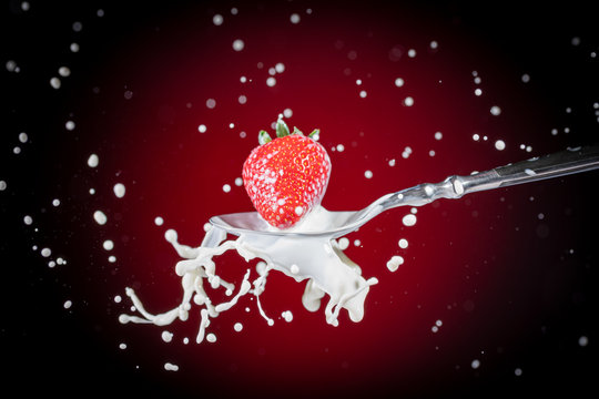 A tasty ripe red Strawberry fall into milk in front of a gradient red backdrop on a tablespoon and are splashed - Strawberry Splash