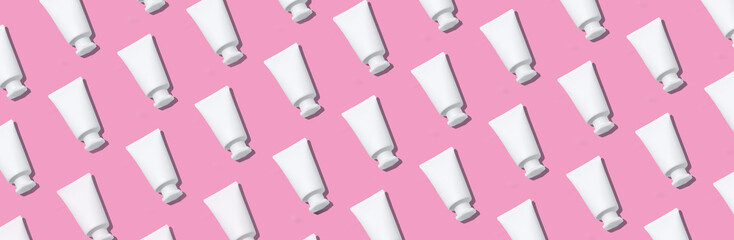 White plastic creams bottles pattern. Cosmetics, skin care, beauty, body treatment concept. Creative design for packaging. Cosmetic jar, tube, bottle on pink background. Top view. Flat lay. Mock-up.
