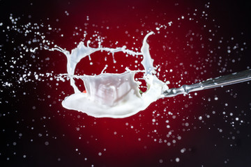 A tasty ripe red Strawberry fall into milk in front of a gradient red backdrop on a tablespoon and...
