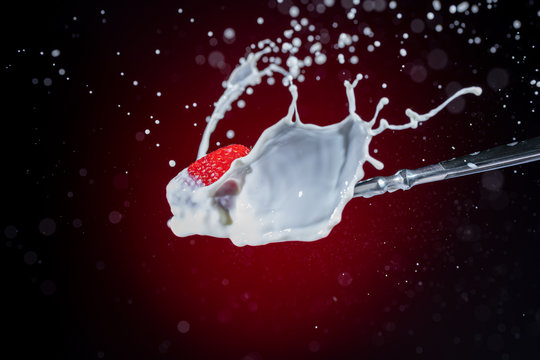 A tasty ripe red Strawberry fall into milk in front of a gradient red backdrop on a tablespoon and are splashed - Strawberry Splash