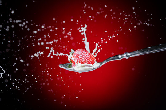 A tasty ripe red Strawberry fall into milk in front of a gradient red backdrop on a tablespoon and are splashed - Strawberry Splash