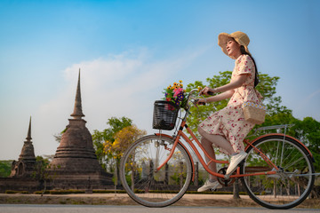 Woman traveller riding retro bicycle enjoy sightseeing takes a picture photo and looks at the buddhist statue with gentle pay respect pray to buddhist statue in historic park of Thailand