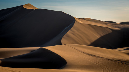 Path along stunning beige dunes outside in the desert with soft sunlight throwing shadows in the peaceful dusk. © Kris Hoobaer