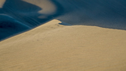 wind blowing beige sand grains over the ridge of a dune. blurred motion in the foreground and...