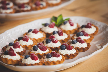 Delicious homemade tartlets with vanilla butter cream and organic blueberries and raspberries on top. Delicious sweet dessert for a party or celebration. Selective focus. Toning
