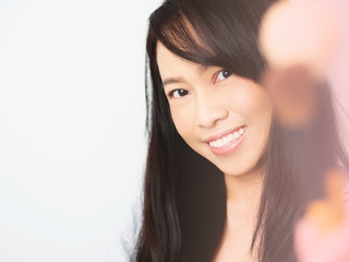 Asian women wearing gray T-shirts are smiling happily. Lady is holding make-up brush extending to camera. Female has dark brown long hair is cheerful and make up pink nude tone color. Soft blurred.