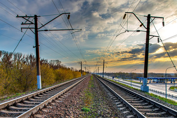 Obraz premium Railway at sunrise. Industrial landscape with railroad, colorful blue sky with red clouds, sun, trees and green grass. Heavy industry. Morning in spring.