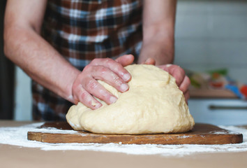 A man in an apron kneads the dough on a wooden board. Hands close up