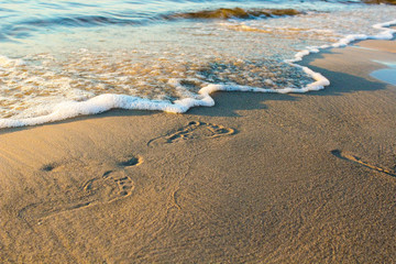 Footprints in send on a beach. Freelance workplace. White sand on the beach of luxury hotel, sunny day. Footprints on the sand with wave of sea foam closeup. Vacation on island in paradice. ..