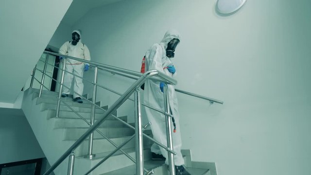 Men in protective suits disinfect stairs with sprayers.