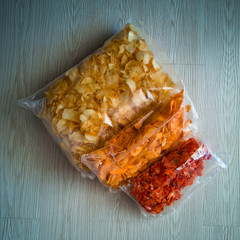 Variety Salty Kerepek Chips Food in a plastic packaging container on a wooden floor.