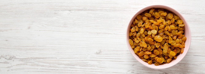 Golden Raisins in a Pink Bowl on a white wooden surface, top view. Flat lay, overhead, from above. Space for text.