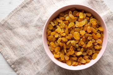 Golden Raisins in a Pink Bowl on a white wooden table, top view. Flat lay, overhead, from above. Copy space.