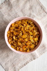 Golden Raisins in a Pink Bowl on a white wooden background, top view. Flat lay, overhead, from above.