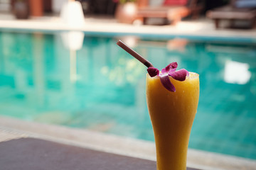 Mango smoothie in a tall glass on the background of the pool