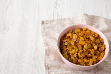 Golden Raisins in a Pink Bowl on a white wooden background, low angle view. Copy space.