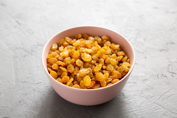 Golden Raisins in a Pink Bowl on a gray background, side view.