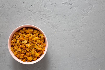 Golden Raisins in a Pink Bowl on a gray background, top view. Flat lay, overhead, from above. Copy space.