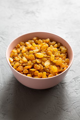 Golden Raisins in a Pink Bowl on a gray background, low angle view.