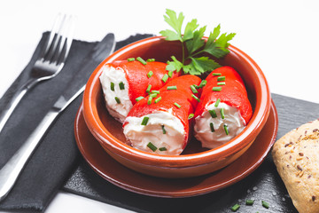 Stuffed piquillo peppers in earthenware casserole on white background.