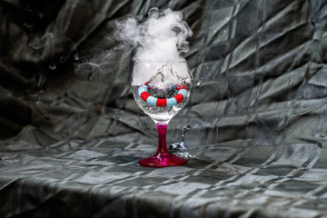 Glass of water with vape smoke and wheel in it. Dark grey background