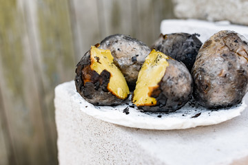 Baked in the fire potatoes in the skin according to the village recipe and method, directly in the ashes. Charred, fragrant tubers, a hot dish on a white stone plate