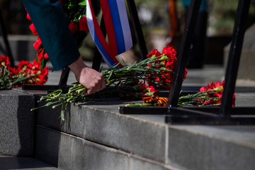 A hand puts red carnations on a granite gravestone. Memory of the dead