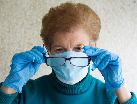 Senior Woman With Mask And Medical Gloves Putting On Glasses