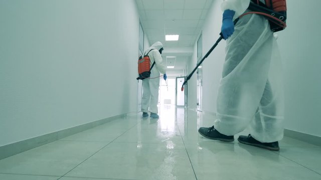 People in hazmats clean hallway, using sprayers.