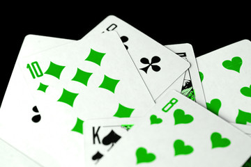 Playing cards unusual green color scattered on a black surface close-up. Gambling background