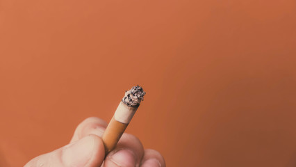 smoldering cigarette in his hand on an orange background