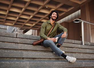 Handsome young man eating sandwich while sitting on stairs during break while looking away