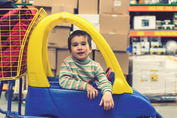 The boy 4 years in a striped jacket is sitting in a children's typewriter in a construction shop. toned