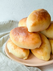 Beautiful and rosy pies on a plate close-up on a light background side view. Fragrant homemade cakes.