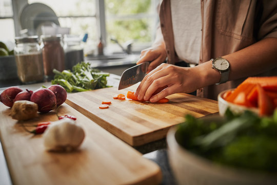 Closeup of young female hands chopping fresh orange carrot on board while in modern kitchen - healthy food to boost the immune system 