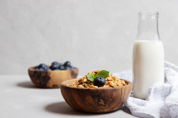 A wooden bowl with homemade granola or oatmeal granola, next to a cup with blueberries and a bottle...