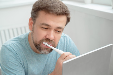 man brushing teeth electric brush looking  mirror
