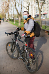 Young man on a bicycle in a medical mask in a city park. Concept of health and safety life from coronavirus pandemic.	