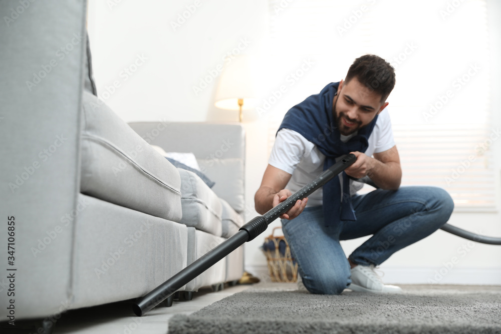 Wall mural young man using vacuum cleaner at home