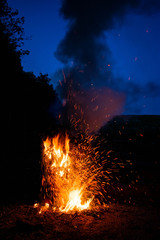 A bonfire raging against a dark blue night sky.  Embers and sparks flying off in all directions.  High red hot flames.
