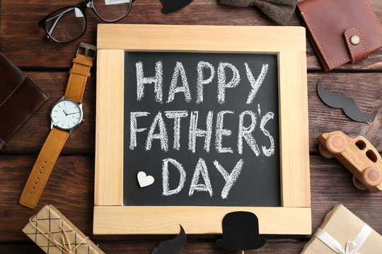 Blackboard with words HAPPY FATHER'S DAY and male accessories on wooden background, flat lay