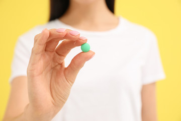 Young woman with vitamin pill on yellow background, closeup