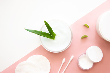 Jars of facial cream with aloe vera extract, cotton pads and buds flat lay on white and pink background top view with copy space. Beauty skincare, natural cosmetic, daily products. Stock photo.