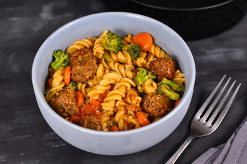 Fusilli pasta, meatballs, broccoli and carrot vegetable bowl and on dark table