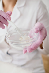 Beautician prepares a white clay face mask in a glass cup. Selective focus